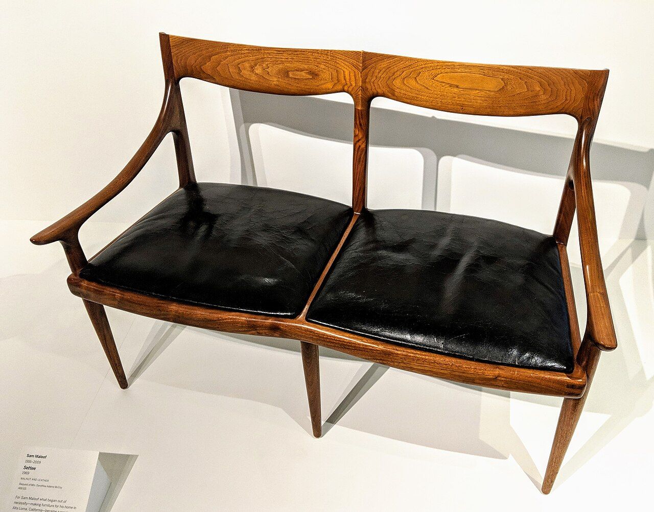 A walnut and leather settee with curved arms made by Sam Maloof