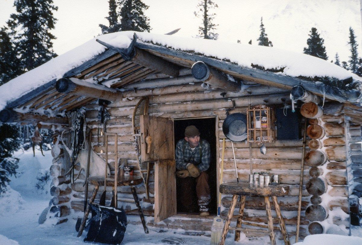 Dick Proenneke sitting in the doorway of his log cabin in the snow